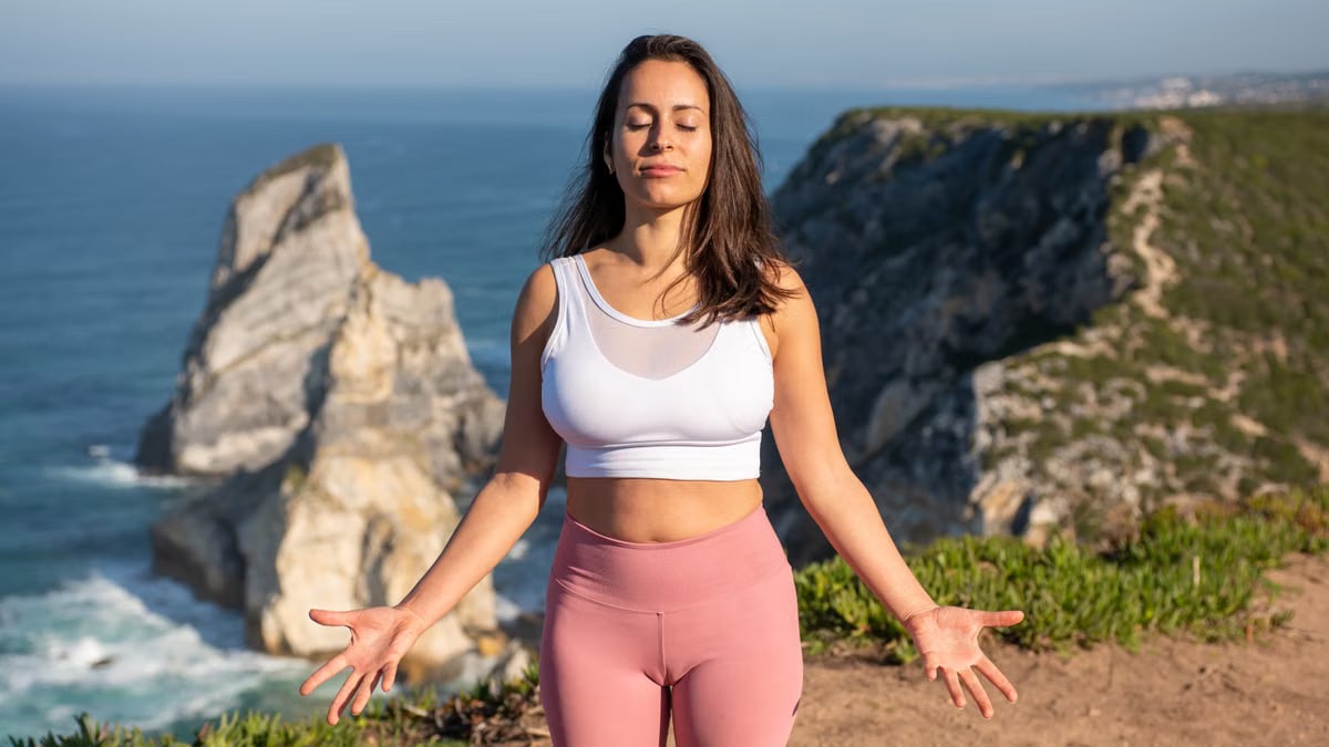 A woman in activewear practices meditation by the sea on a sunny day in Portugal.